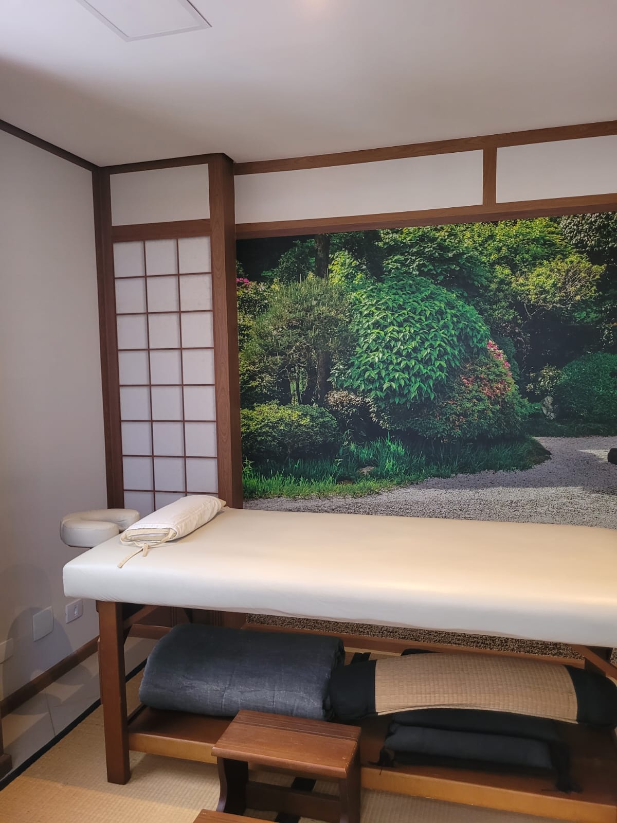Sala de massagem com maca e mural de jardim japonês
